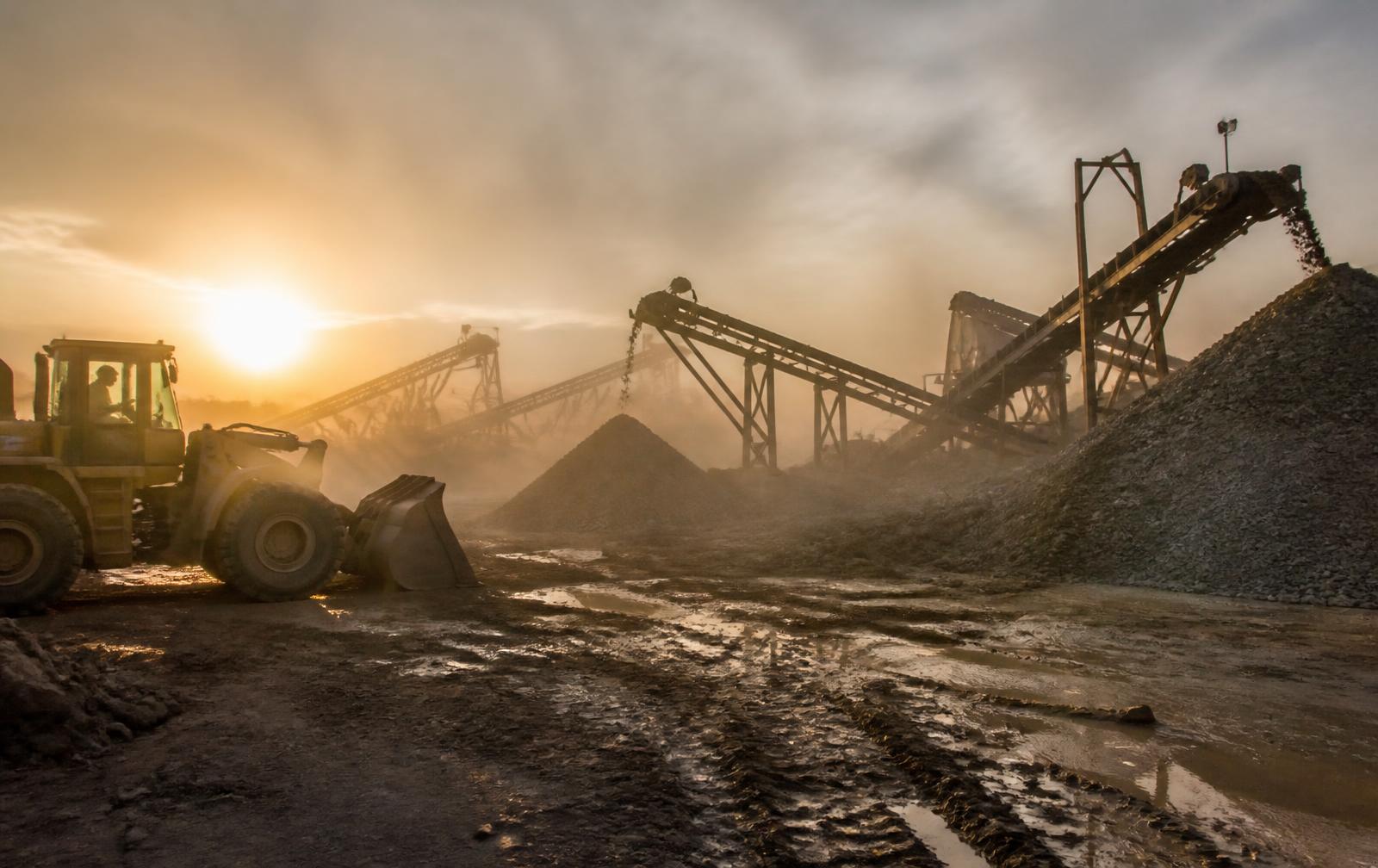 Deltarsa's mining and crushing operation at dusk — conveyors, aggregate stockpiles, dust in warm light